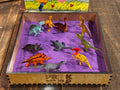 Sensory tray filled with toy dinosaurs and purple sand, fostering early learning through sensory bin play and fine motor skill activities.