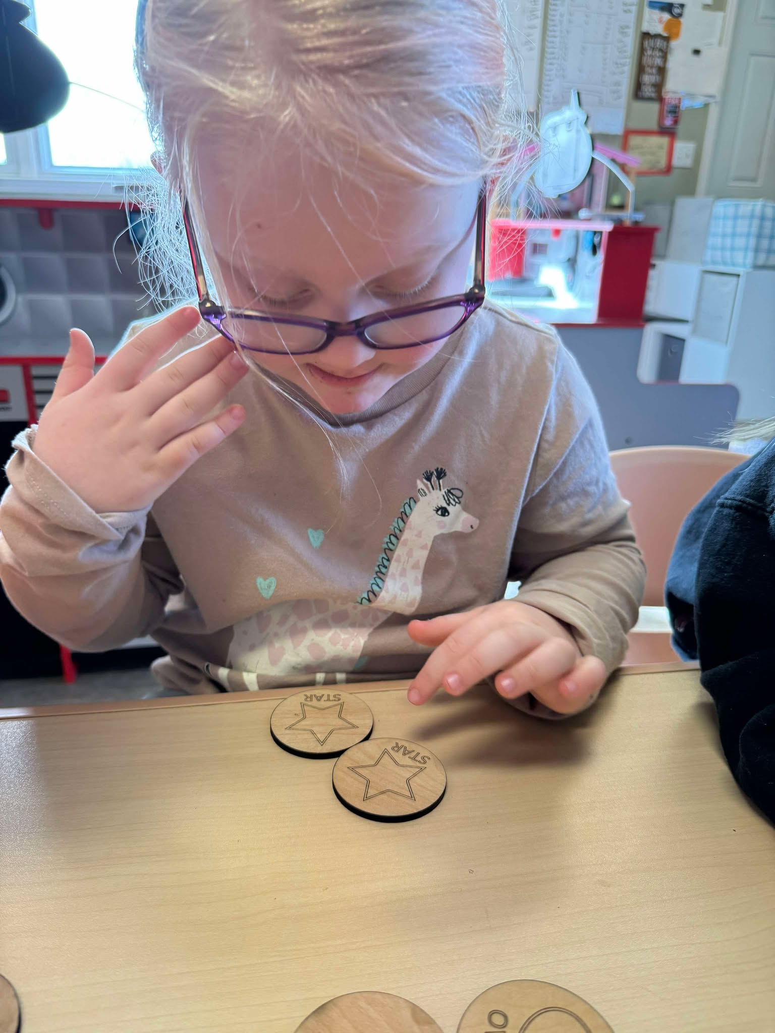 Young girl intently matching wooden shape tiles from the Basic Shapes Matching Game, developing visual memory and concentration through hands-on play. Perfect for social-emotional learning in preschool and homeschool