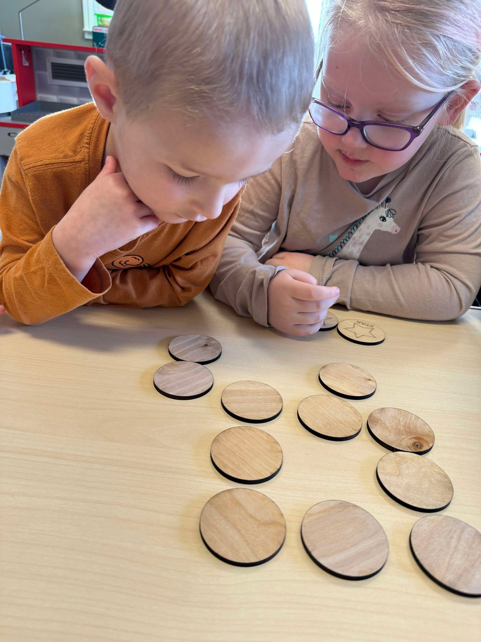 Focused preschoolers playing with the Basic Shapes Matching Game, flipping over wooden shape tiles to encourage critical thinking and hand eye coordination in a structured learning environment.